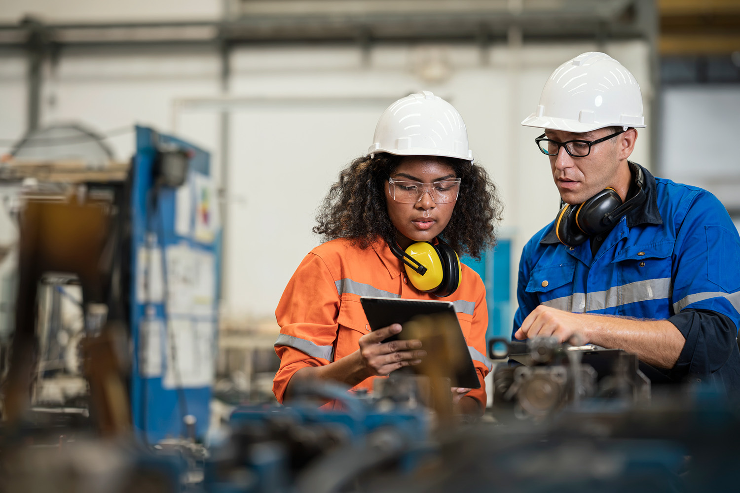 African american woman and caucasian male using an ipad to discuss next steps at a manufacturing facility.